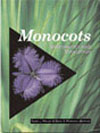 The cover image of Monocots: Systematics and Evolution, featuring a purple flower against a plain black background, set into a cover of tall green gra